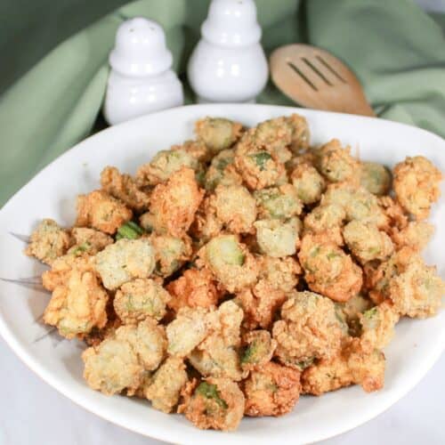 Fried okra in a white dish with a green tablecloth and white salt and pepper shakers.