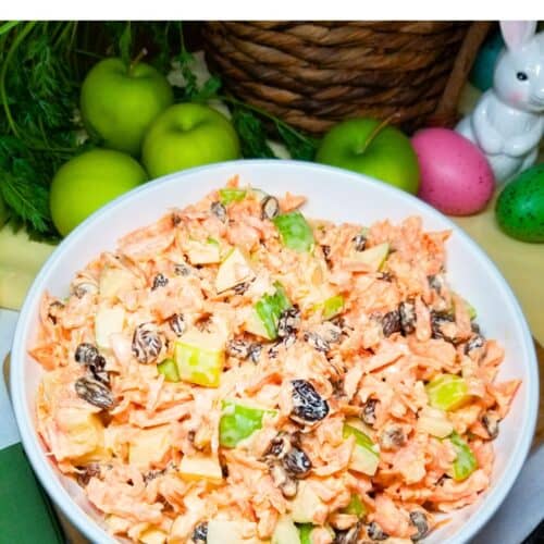 Carrot Apple Salad with raisins in a white bowl sitting on a farmhouse table.