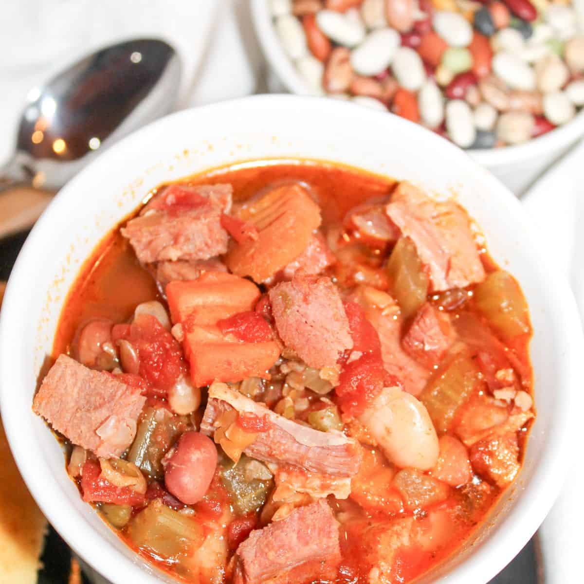 Ham and bean soup in a white bowl with a spoon and dried beans in the background.