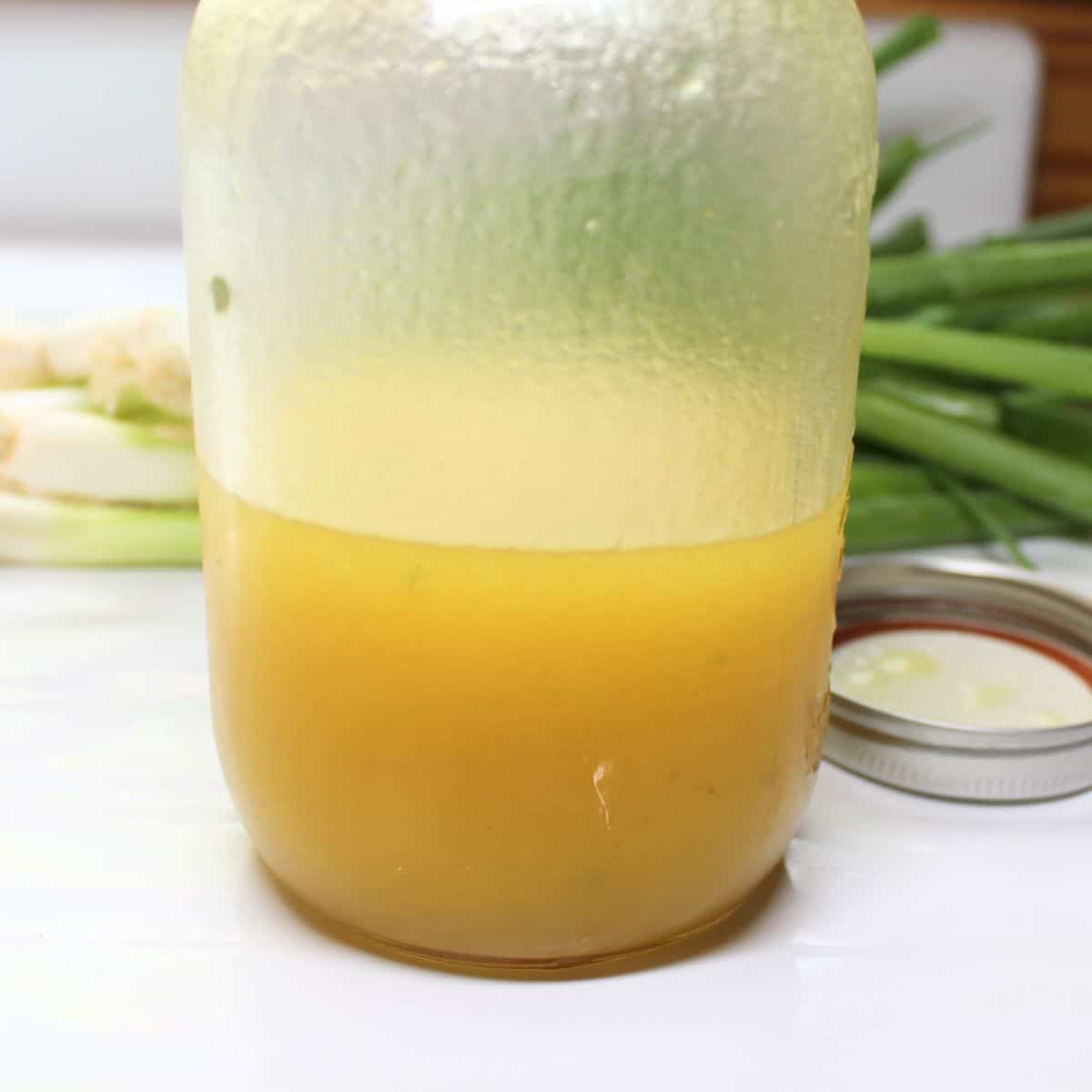 Mixed dressing for the coleslaw in a Mason jar. Green onions in the background.