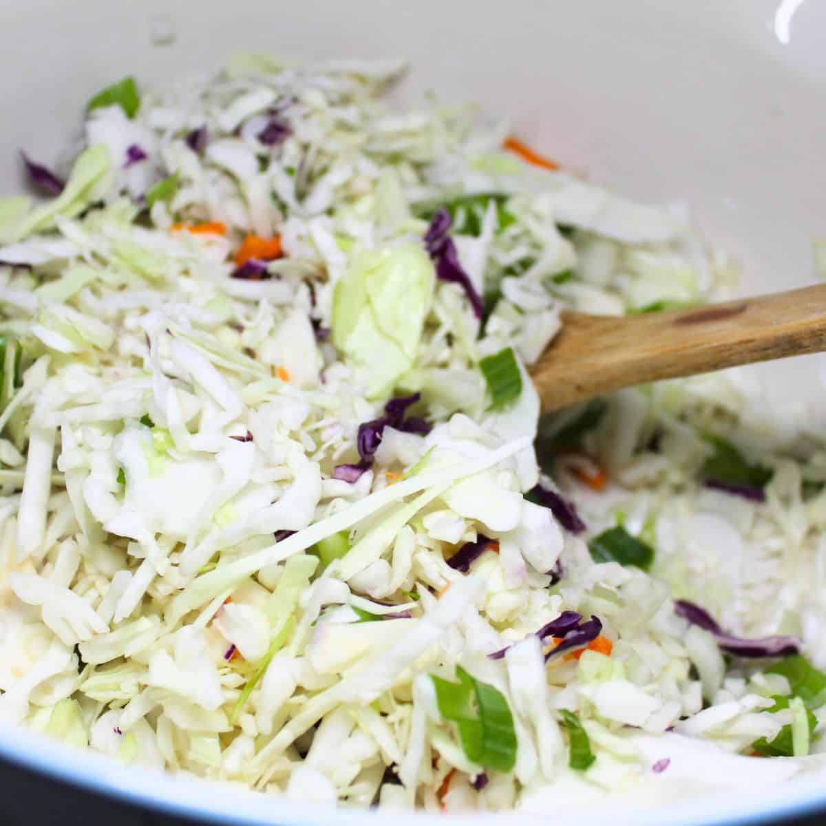 Coleslaw mix and green onions in a bowl with a wooden spoon.