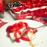 American Flag Cheesecake garnished with fresh strawberries, blueberries on top of pie filling and a slice of cheesecake on a plate.