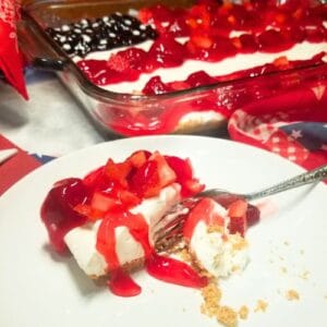 American Flag Cheesecake garnished with fresh strawberries, blueberries on top of pie filling and a slice of cheesecake on a plate.