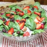 Spinach salad in a bowl with a red and white dish towel on the bottom of the bowl.