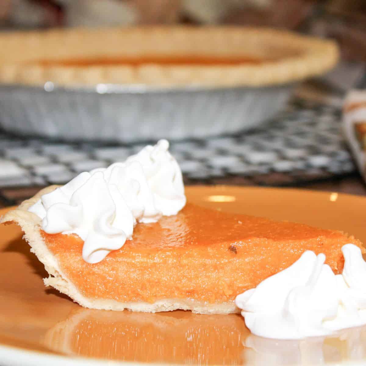 A slice of sweet potato pie on a brown plate and a whole pie cooling on a wire rack.