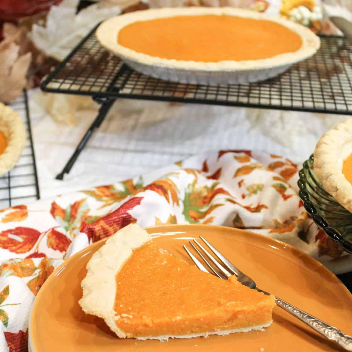 A slice of sweet potato pie on a brown plate and a whole pie cooling on a wire rack.