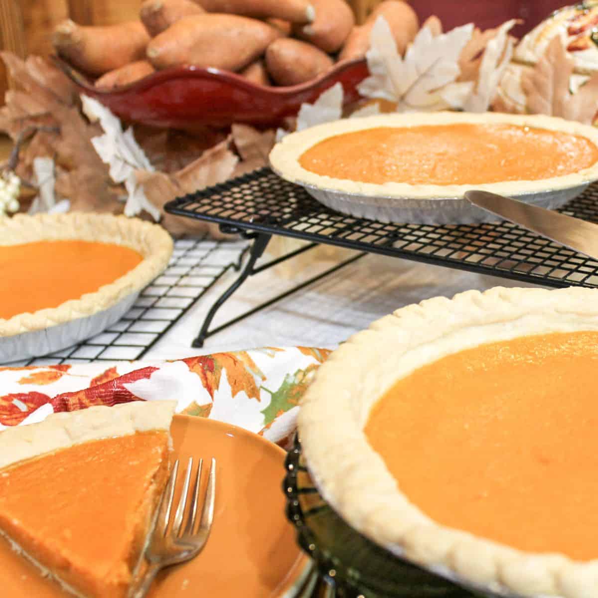 Whole sweet potato pies and a slice of pie on a brown plate with a fork.