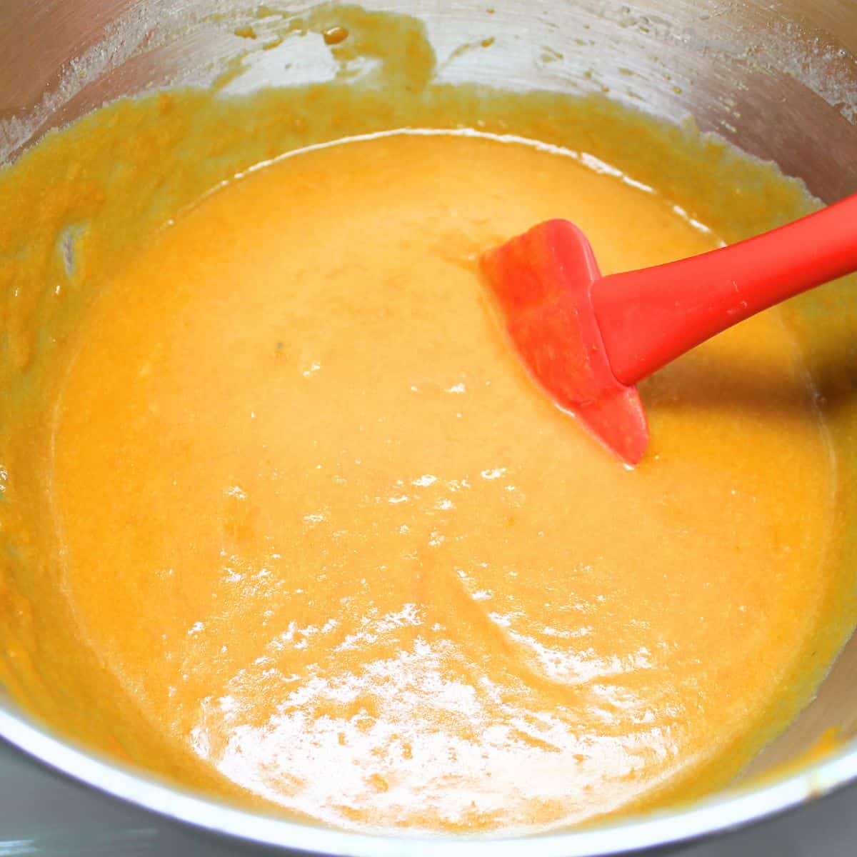 Sweet potatoes mixed with other ingredients in a mixing bowl. Red spoon.