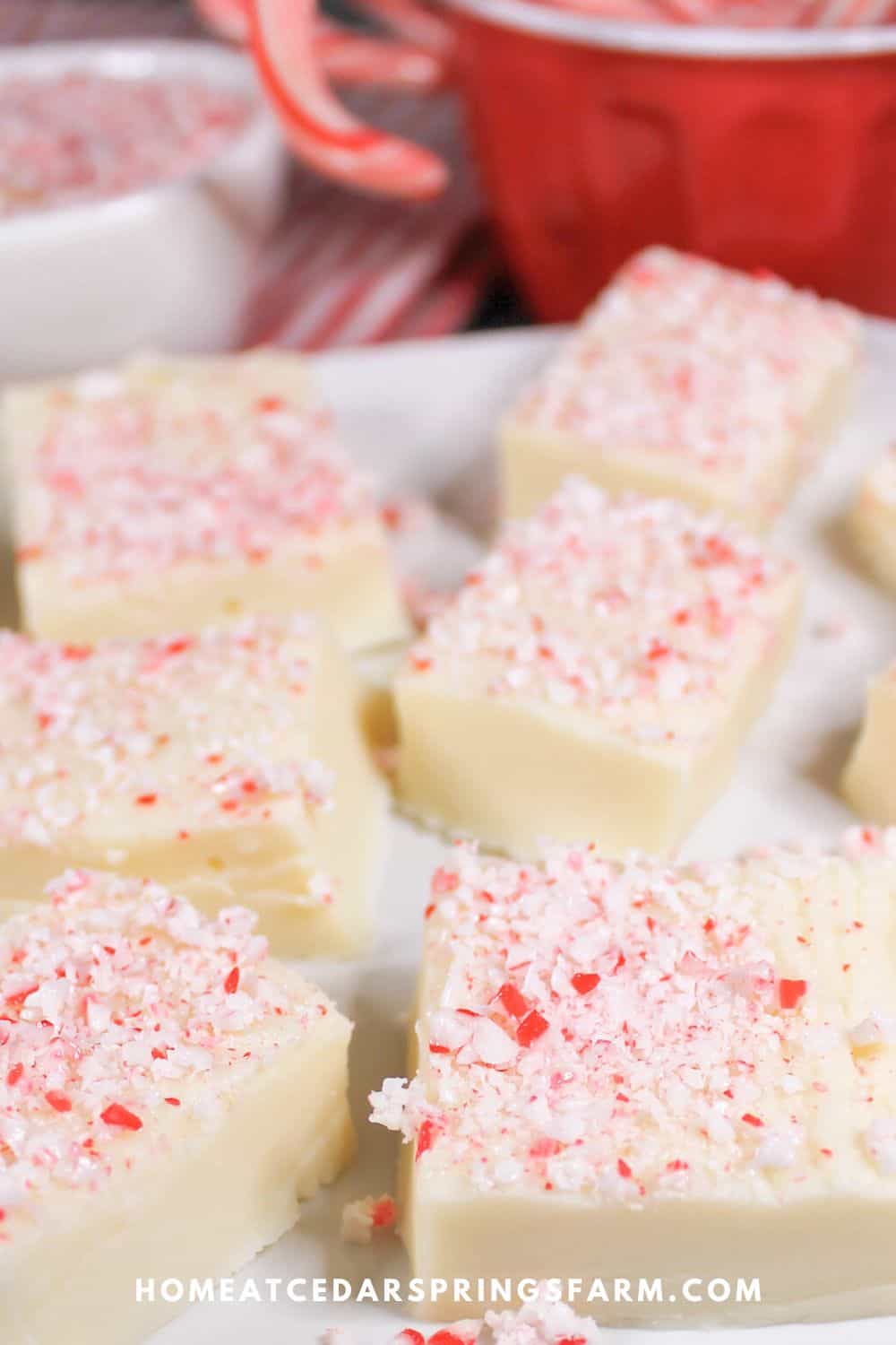 White chocolate peppermint fudge on a white plate with peppermint candies in other dishes.