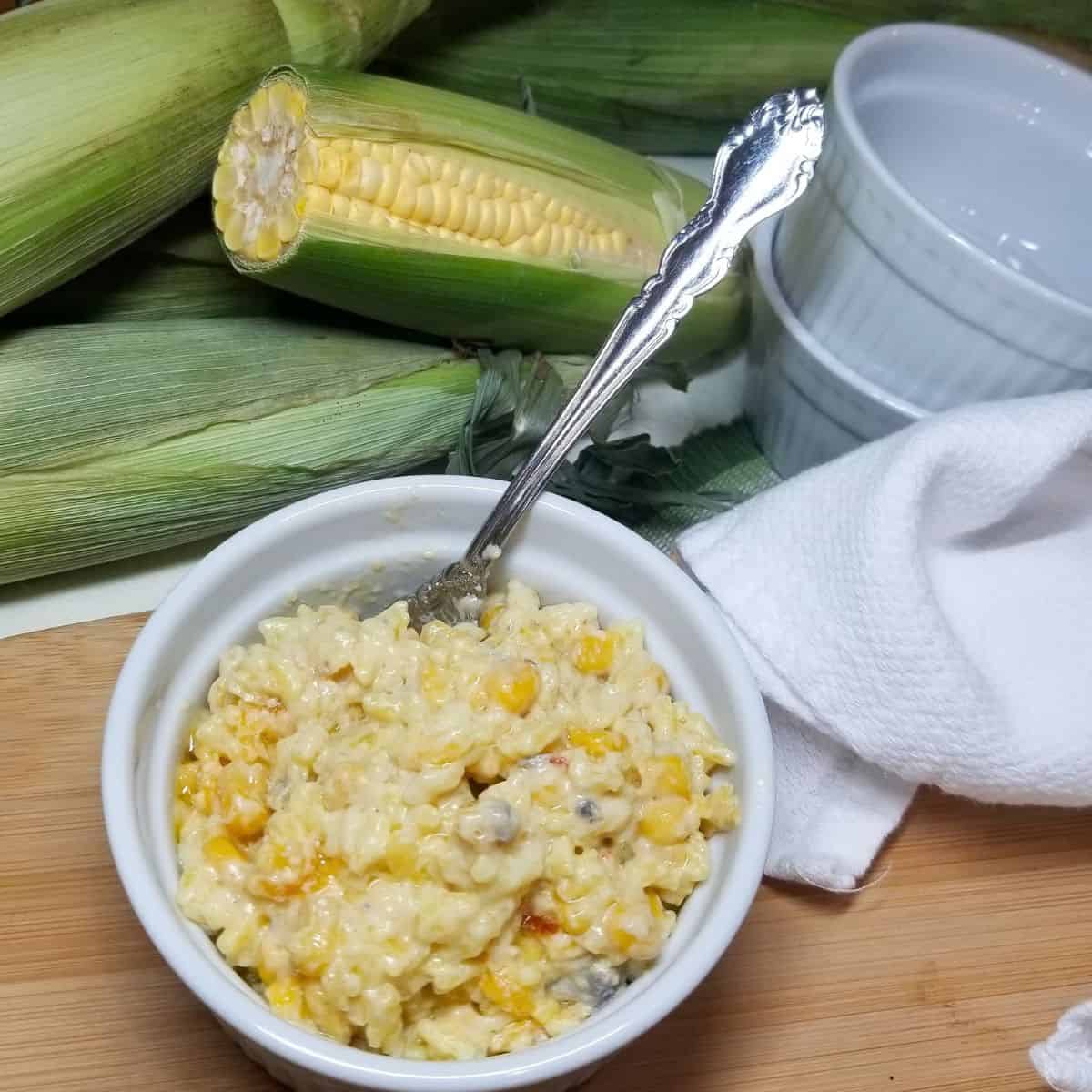 Yellow rice and corn casserole in a white serving bowl with corn in the background.